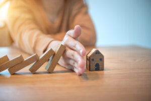 An image of a woman stopping dominoes from falling onto a small house; concept of disaster management for our article on salary for MPH holders